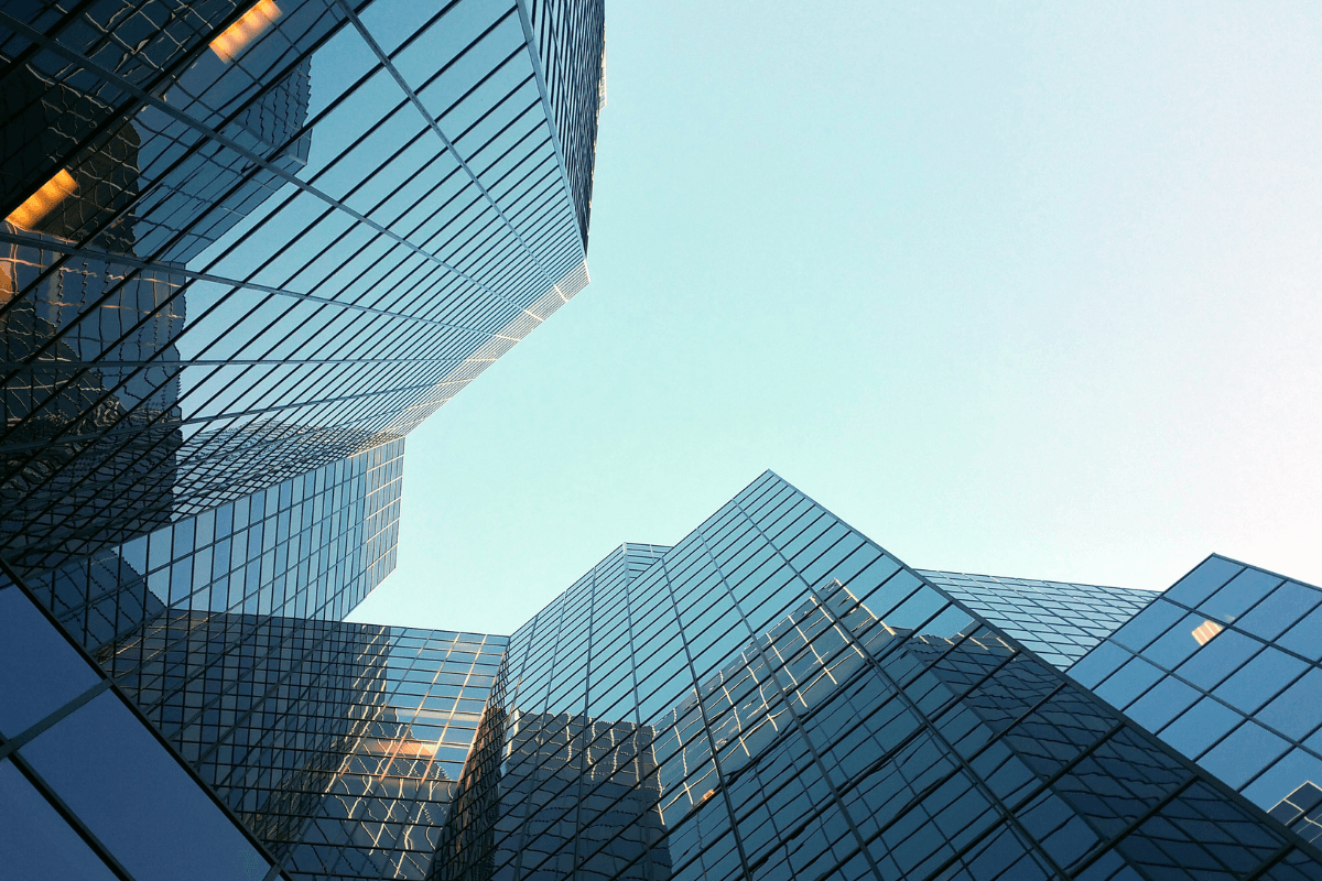 Perspectiva contrapicada de rascacielos de vidrio modernos reflejando el cielo azul y luz cálida.