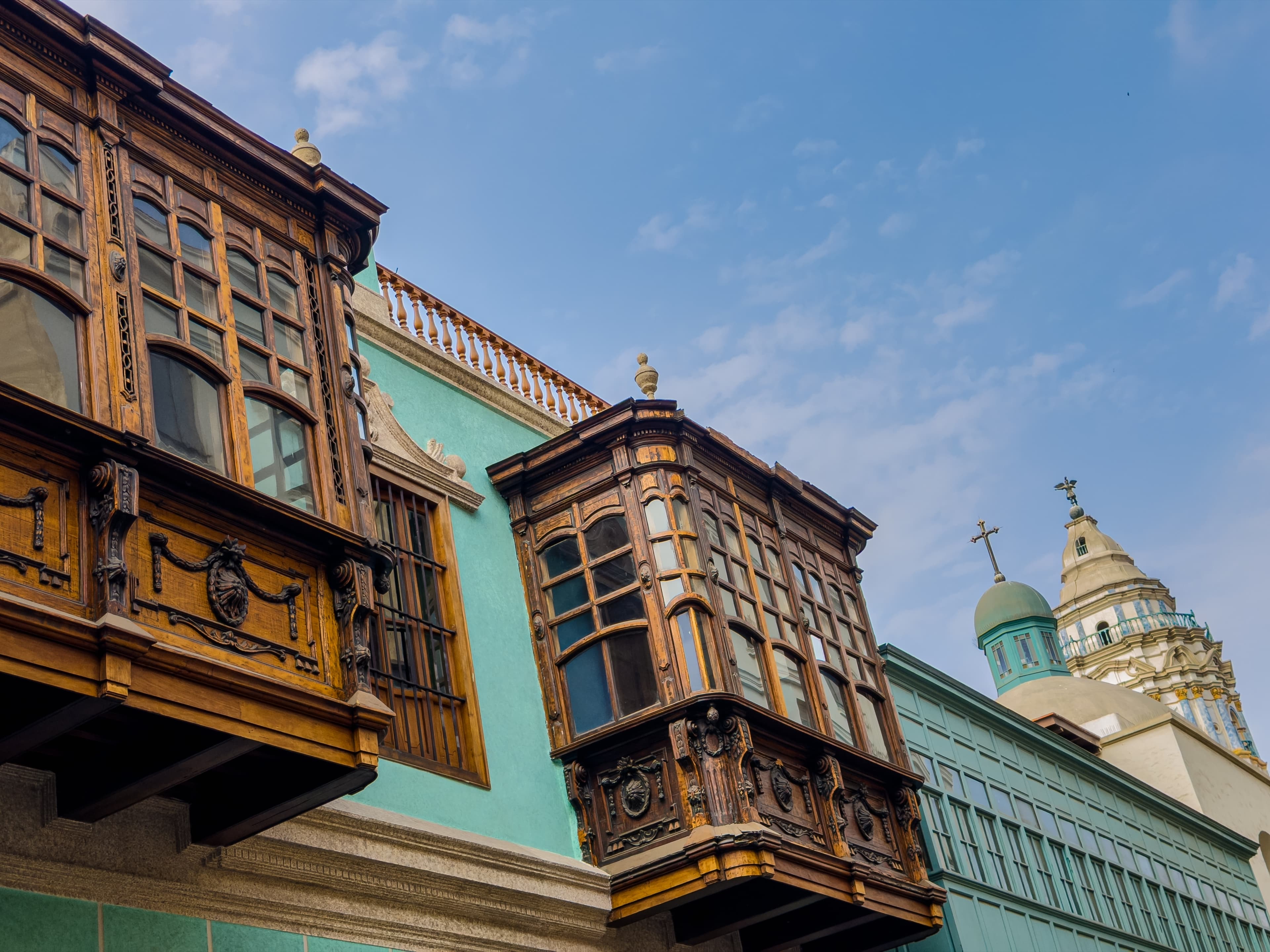 Balcones de madera tallada en edificios coloniales con una cúpula de iglesia al fondo.