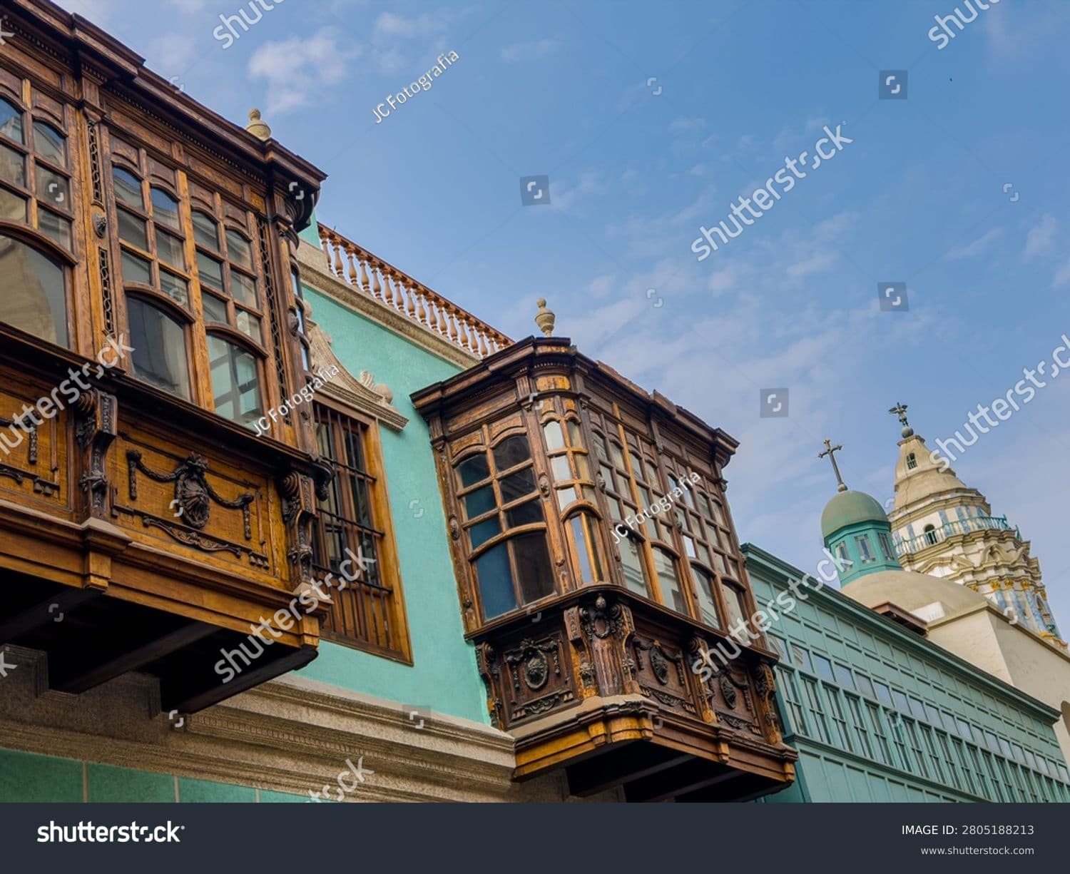 Balcones coloniales de madera tallada en un edificio verde con una cúpula al fondo.